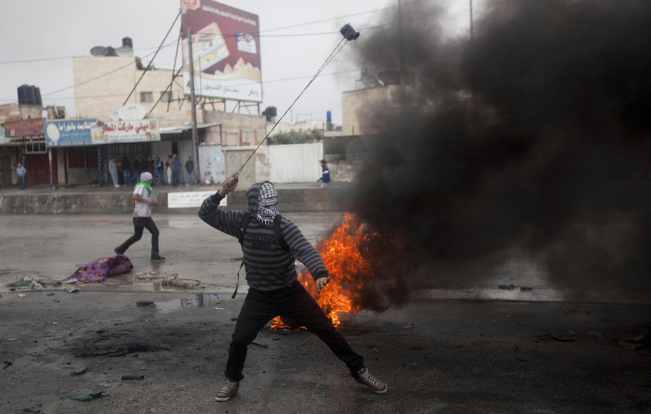 Um palestino usa um estilingue durante confrontos com soldados israelenses no posto de controle de Qalandia, perto da cidade de Ramallah, Cisjordânia