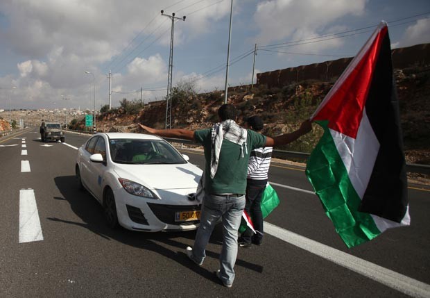 Jovens palestinos bloqueiam estrada entre Ramallah e Nablus, usada por colonos israelenses, para protestar nesta segunda-feira (19) contra a ação israelense na Faixa de Gaza (Foto: AFP)