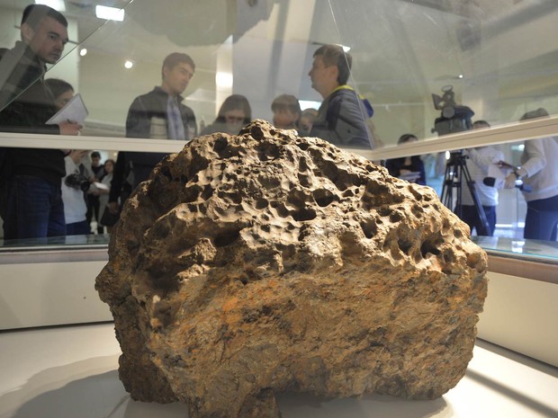 Jornalistas observam pedaço de meteorito exposto em um museu de Chelyabinsk, na Rússia. Segundo as autoridades, a rocha retirada do fundo do Lago Chebarkul é o maior parte do meteorito que causou estragos e deixou cerca de mil feridos em fevereiro. (Foto: Andrey Tkachenko/Reuters)