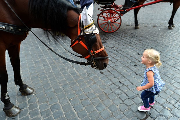 Menina se aproxima do cavalo de uma carruagem de passeio turístico no centro histórico de Roma, na Itália (Foto: Alberto Pizzoli/AFP)