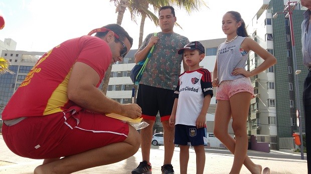 Família de turistas recebe pulseirinha de bombeiro na Jatiúca (Foto: Derek Gustavo/G1)