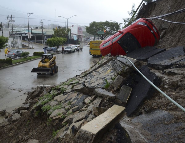 Um carro de rodas para cima é visto em cima de uma montanha que desabou na cidade de Acapulco, no Mexico, neste domingo (15). Enchentes e deslizamentos ocorreram na região com a passagem no furacão Ingrid e da tempestade tropical Manuel. (Foto: Bernandino Hernandez/AFP Photo)