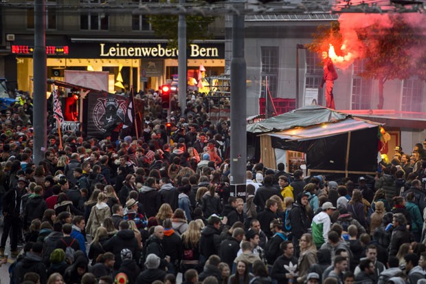 Homem é visto com sinalizador em meio a multidão que participava de 'parada techno' em Berna, capital da Suíça.  (Foto: Fabrice Coffrini/AFP)