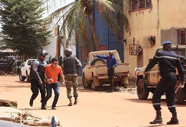 Policial malinês acompanha um dos reféns libertados no hotel Radisson Blu (Foto: Harouna Traore/AP)