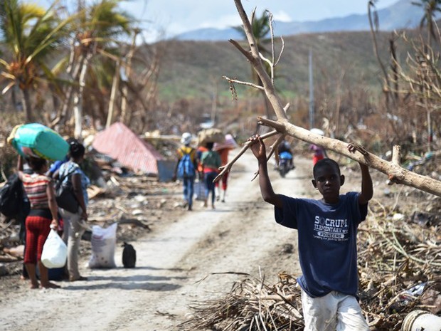 Pessoas caminham por rua de Les Cayes, no Haiti, na segunda-feira (10). Cidade ficou devastada após a passagem do furacão Matthew  (Foto: Hector Retamal / AFP)