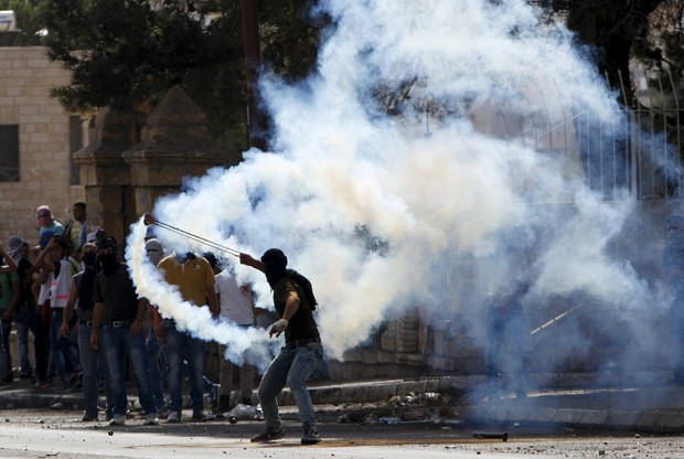 Palestino atira de volta uma bomba de gás lacrimogêneo lançado por soldados israelenses durante confrontos em Belém (Foto: Mussa Qawasma/Reuters)