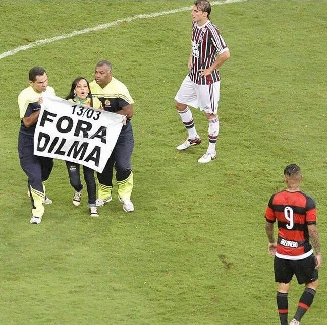 O Fla-Flu no Estádio Manoel Garrincha, em Brasília, foi interroimpido por uma mulher que invadiu o campo com um cartaz onde estava escrito "Fora Dilma". Durante três minutos, quase todo o estádio gritou "Fora, Dilma (Foto: Redes Sociais)