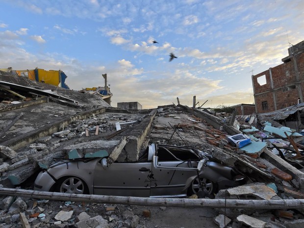 Carro esmagado é visto sob destroços de um prédio que desabou devido ao terremoto em Manta, no Equador (Foto: Luis Acosta/AFP)