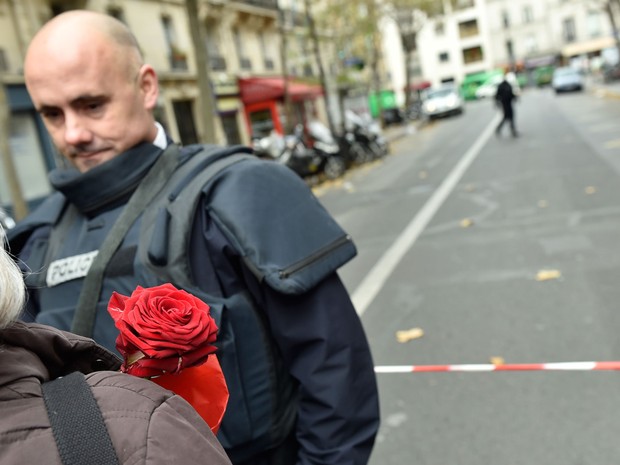 Civil com rosa na mão conversa com policial na Rua de Charonne em Paris, neste sábado (14)  (Foto: AFP)