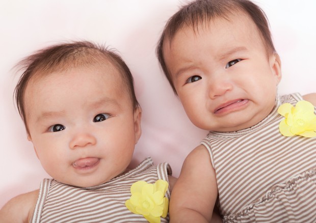 Two twin Asian baby girls, Chinese infants with different expressions and moods. One is happy and cheerful, the other sad and crying. They are between 0-6 months old and wear matching dresses as they look up at the camera. A cute portrait of beautiful sis (Foto: Getty Images)