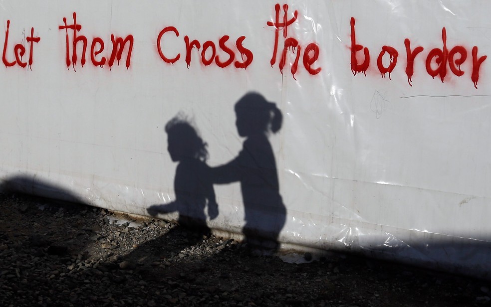 Sombras de crianças são vistas em uma barraca com a frase 'Let them cross the border' (Deixam eles cruzarem a fronteira) escrita no local onde imigrantes e e refugiados acampam em Idomeni, na fronteira da Grécia com a Macedônia (Foto: Gregorio Borgia/AP)
