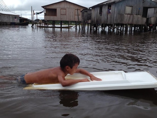 Criança se apoia em porta de geladeira durante enchente em Cruzeiro do Sul  (Foto: Genival Moura/G1)