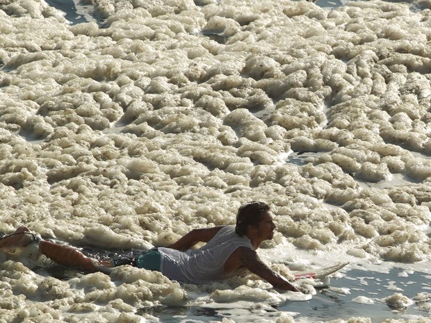 Surfista rema em meio à grossa espuma que invadiu a orla principalmente perto do final da Praia do Leblon, próximo à Av Niemeyer, na Zona Sul do Rio de Janeiro. (Foto: Gabriel de Paiva/Agência O Globo)