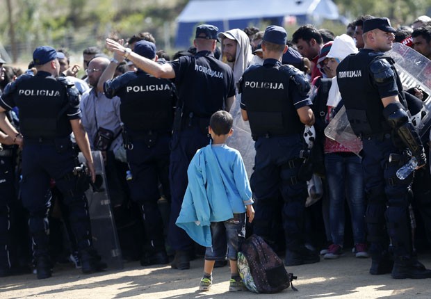 Policiais sérvios observam migrantes que estão cruzando a fronteira entre a Macedônia e a Sérvia (Foto: Darko Vojinovic/AP)