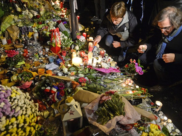 Pessoas acendem velas e depositam flores em frente ao café Belle Equipe, na rue de Charonne, em Paris, na sexta (20). O local foi um dos atacados por terroristas há uma semana (Foto: AFP Photo/Alain Jocard)