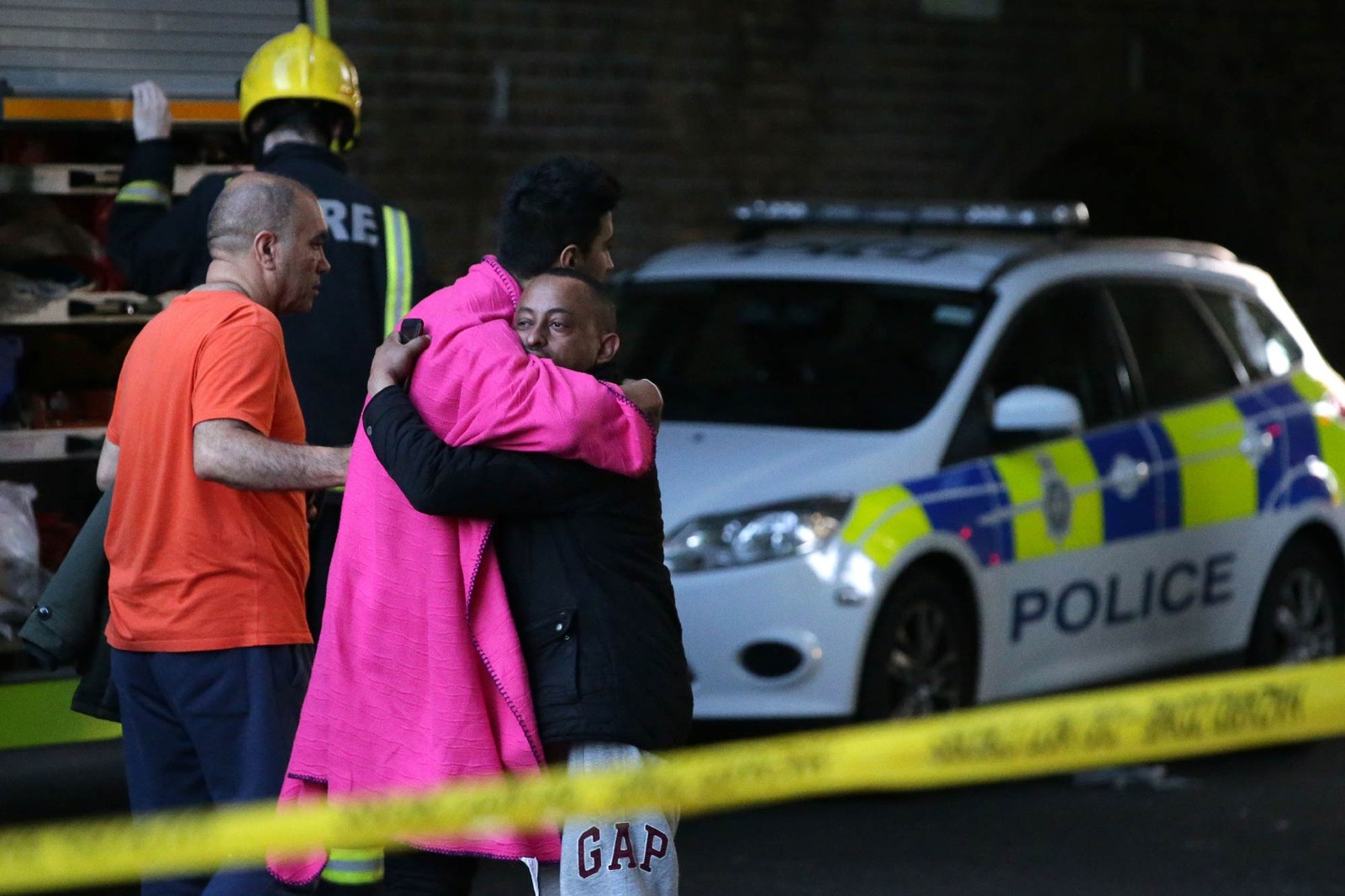 Homens se abraçam do lado de dentro do cordão de isolamento policial enquanto o fogo toma conta da Torre Grenfell, em Londres (Foto: Daniel Leal-Olivas/AFP)