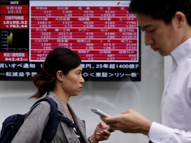 Pedestres passam en frente a painel eletrônico com as cotações da bolsa, em Tóquio, nesta quarta-feira. (Foto: Reuters)