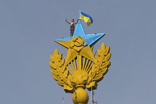 Homem faz selfie junto com bandeira ucraniana hasteada junto à estrela soviética no topo de um arranha-céu em Moscou nesta quarta-feira (20) (Foto: Ilya Varlamov/Reuters)