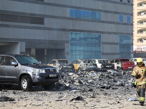 Bombeiro caminha entre carros atingidos por destroços de prédio em chamas em Sharjah, nos Emirados Árabes Unidos, na quinta (1º) (Foto: AP Photo)