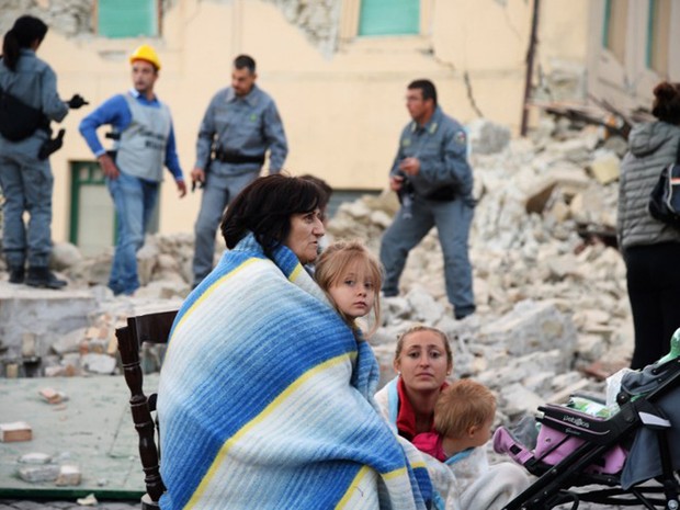 Vítimas de tremor descansam ao lado de destroços de casa, em Amatrice, após tremor que atingiu a região central da Itália nesta quarta-feira (24) (Foto: Filippo Monteforte/AFP)