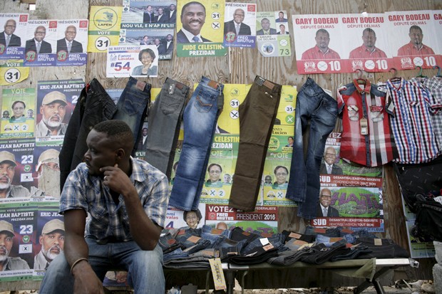 Vendedor de roupas coloca calças e camisas penduradas em frente aos cartazes da eleição presidencial haitiana, que acontece no domingo (25) (Foto: Jossy Ola/AP)