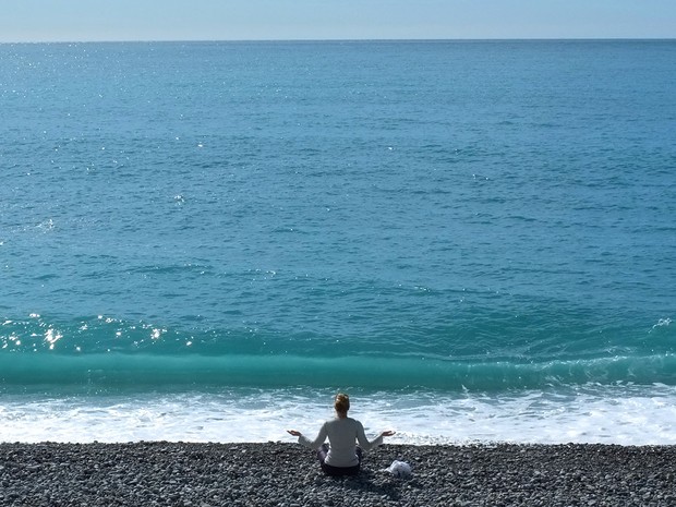 Mulher medita na praia, em Nice. (Foto: Lionel Cironneau/AP)