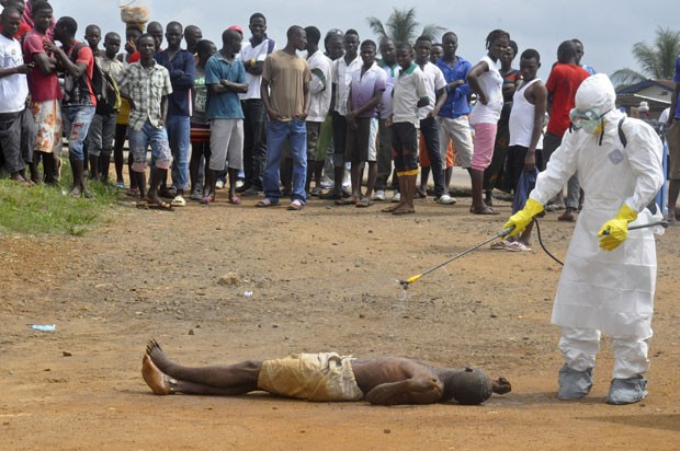 Funcionário de departamento de saúde da Libéria limpa com desifetante um homem que teria morrido por ebola em Monrovia. A imagem é de 4 de setembro (Foto: Abbas Dulleh/AP)
