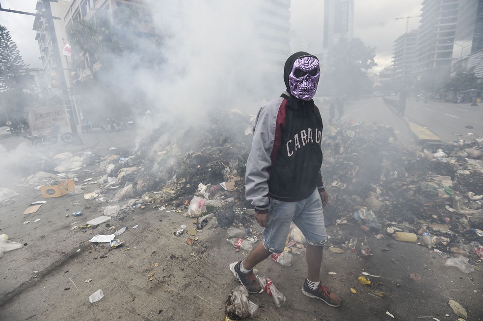 Em foto de 29 de junho, manifestante protesta contra o governo do presidente Nicolas Maduro; barricada de lixo que bloqueia rua em Caracas (Foto: Juan Barreto/AFP)