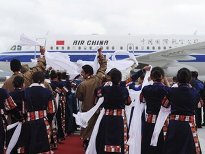 Cidadãos usando roupas típicas tibetanas acenam para os passageiros do primeiro voo no aeroporto (Foto: Reuters/China Daily)