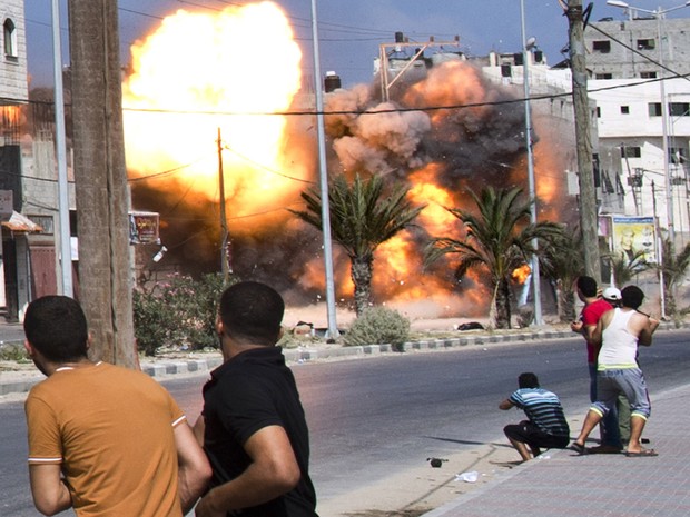 Palestinos observam de perto a explosão de um ataque aéreo israelense a uma casa na Cidade de Gaza (Foto: Roberto Schmidt/AFP)