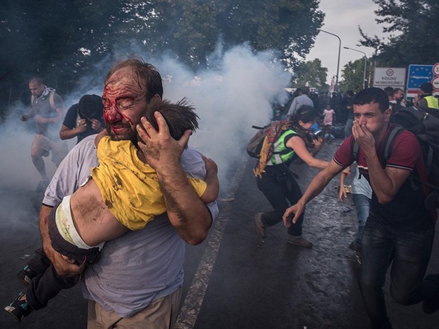 Um homem tenta proteger uma criança após ataque da polícia na fronteira em Horgos, na Sérvia (Foto: Sergey Ponomarev/The New York Times/The Pulitzer Prize)