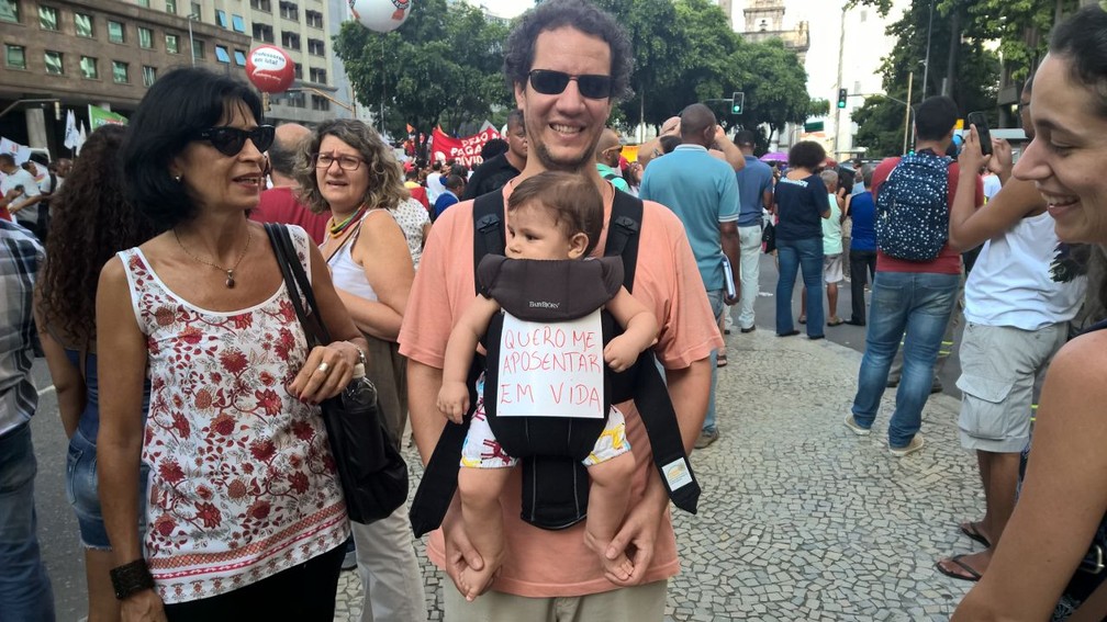 Homem carrega criança com frase: Quero me aposentar em vida (Foto: Carlos Brito/G1)