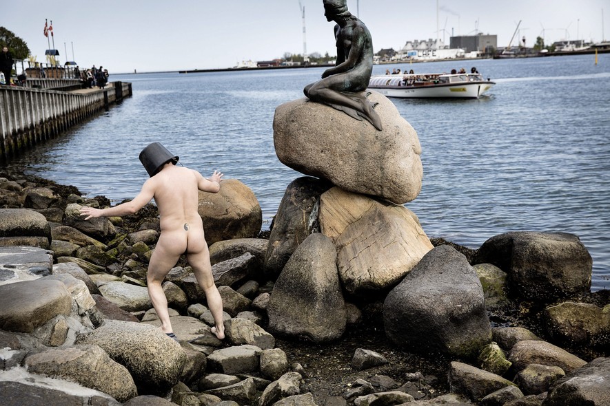 O artista dinamarquês Uwe Max Jensen se apresenta, nu, diante da estátua da Pequena Sereia, um dos pontos turísticos mais famosos de Copenhage