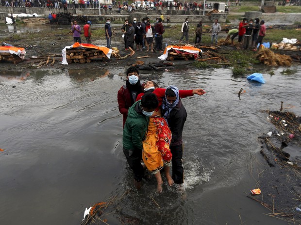 Pessoas carregam uma mulher que desmaiou depois de realizar os últimos rituais com familiares que morreram no terremoto de sábado (25), durante cremação ao longo de um rio em Catmandu, no Nepal (Foto: Adnan Abidi/Reuters)