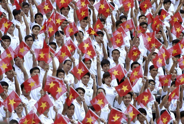 Participantes de desfile agitam a bandeira do Vietnã durante celebração dos 40 anos do final da guerra nesta quinta-feira (30) em Ho Chi Minh (Foto: Dita Alangkara/AP)