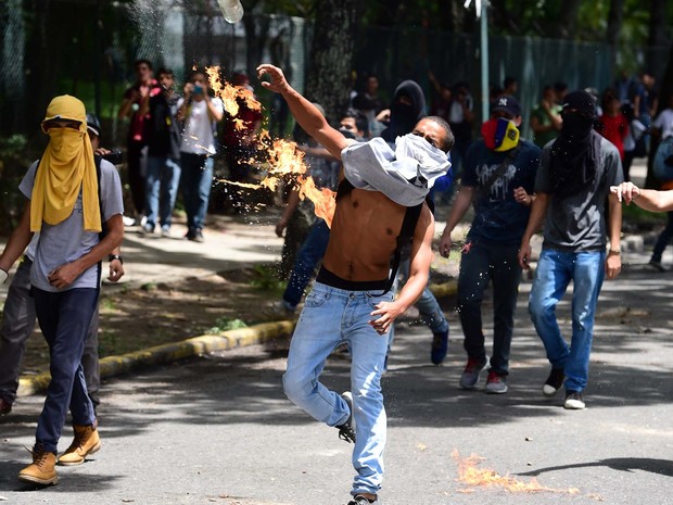 Estudantes universitários da UCV atiram pedras contra cerco policial durante manifestação nesta quinta-feira (9) em Caracas (Foto: RONALDO SCHEMIDT / AFP)