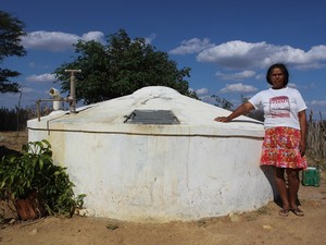Maria Francisca ao lado da cisterna que armazena a água levada pelo carro-pipa (Foto: Patrícia Andrade/G1)