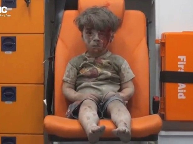O menino Omran Daqneesh, de 5 anos, aguarda atendimento em uma ambulância, sujo de sangue e de poeira, após ser resgatado dentre escombros de um edifício alvo de um bombardeio aéreo em Aleppo, no norte da Síria. A cena causou comoção nas redes sociais (Foto: Reuters)
