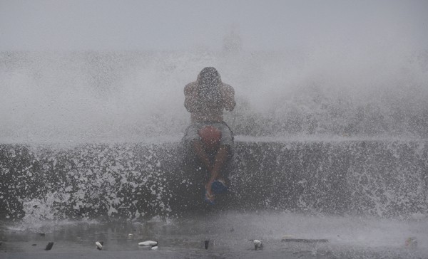 Garoto é atingido por ondas em Manila, capital das Filipinas, neste domingo (14) (Foto: AP)