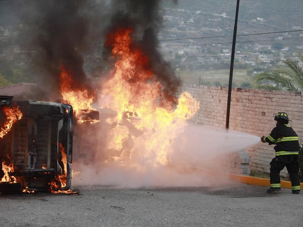 Bombeiro apaga fogo em carros destruídos durante protesto em Guerrero, no México, no domingo (14) (Foto: Reuters/Jorge Dan Lopez)