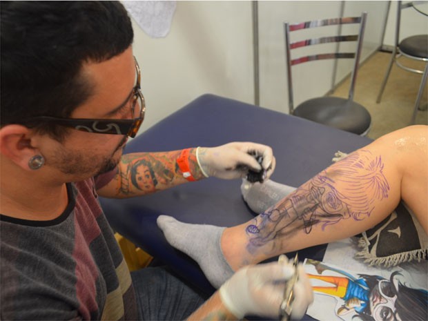 O tatuador Gláuber, do Rio de Janeiro, marca a pele da amiga com uma caricatura do Pe Lanza (Foto: Rodolfo Tiengo/ G1)