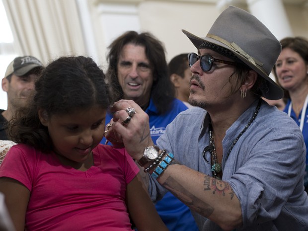 Johnny Depp coloca um aparelho auditivo no ouvido de uma criança, em sua vinda ao Rio (Foto: AP Photo/Silvia Izquierdo)