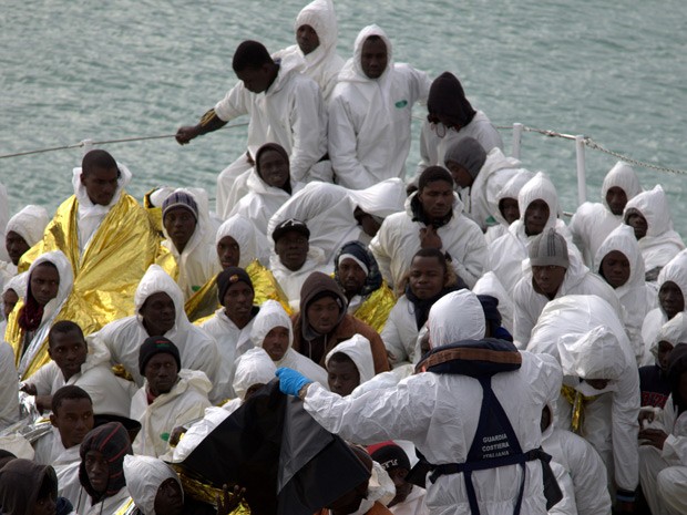 Migrantes esperam para desembarcar de um navio da Guarda Costeira italiana depois de serem resgatados no Mediterrâneo neste sábado (Foto: AP Photo/Francesco Malavolta)