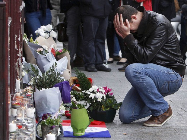 Homem se emociona diante de objetos de tributo deixados em frente à cafeteria Carillon, em Paris, onde um dos ataques terroristas ocorreu (Foto: Thibault Camus/AP)
