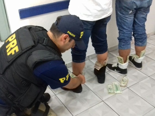 Policial recolhe dólares sem origem comprovada em meia de homem (Foto: Polícia Rodoviária Federal / Divulgação)
