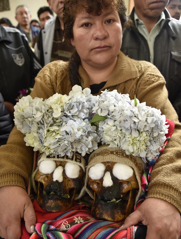  Mulher deixa cemitério de La Paz, na Bolívia, neste domingo, carregando dois crânios humanos na celebração do Dia das Ñatitas (Foto:  AFP Photo/Aizar Raldes)