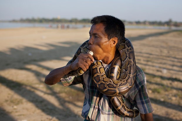 Um encantador de cobras colocou a cabeça de uma píton dentro de sua boca na tentativa de atrair turistas perto ponte histórica de U Bein em Amarapura, em Mianmar (Foto: Hkun Lat/AP)