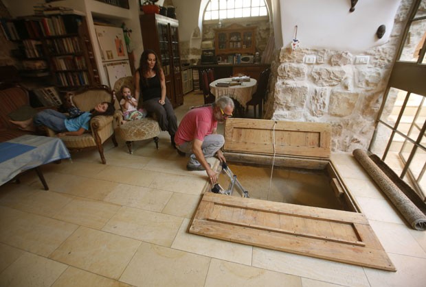 Tal mostra o alçapão no chão de sua sala, que leva até o banheiro de 2 mil anos descoberto no subterrâneo, em Jerusalém (Foto: Gali Tibbon/AFP)