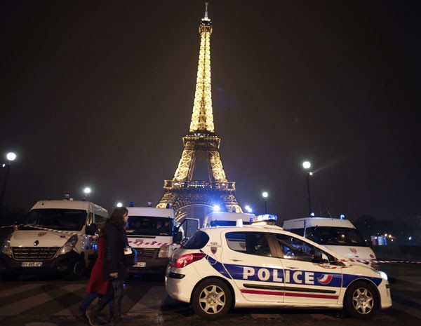 Pessoas passam por carros de polícia que bloqueiam o caminho para a Torre Eiffel Tower, neste sábado (30), após ameaça de ataque ao monumento. (Foto: Thomas Coex/ AFP Photo)