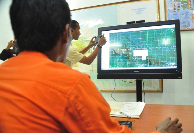  Funcionários do sistema nacional de busca e resgate da Indonésia analisam mapa do terreno onde avião se acidentou neste domingo (16)  (Foto: Indrayadi/AFP)
